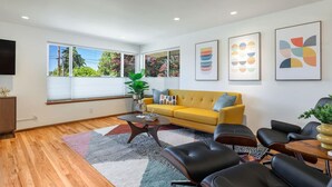 Ein modernes Wohnzimmer mit einem gelben Sofa, schwarzen Ledersesseln, einem Couchtisch und abstrakter Wandkunst.