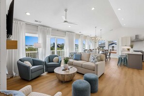 A spacious living area with a sofa, armchairs, ottomans, a coffee table, and a dining area with chairs and a table.
