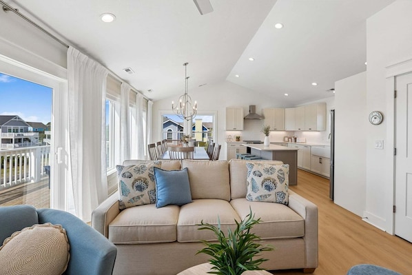 A modern living room with a sofa, dining table, and kitchen in the background.