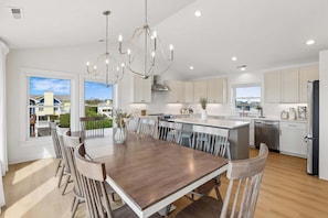 A modern kitchen with a central island, white cabinetry, and a dining area with a wooden table and chairs.
