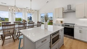 A modern kitchen with a large island, stainless steel appliances, and a view of the neighborhood. - 1726 - Beach Sea Sun - Dog-Friendly Corolla Getaway | Pool & Hot Tub (Corolla)