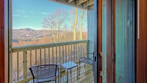A wooden deck with a glass door leading to a balcony overlooking a mountainous landscape.