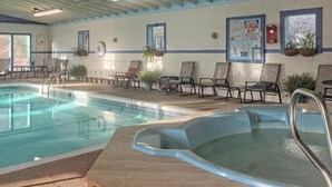 A pool area with a hot tub, lounge chairs, and a lifeguard warning sign.