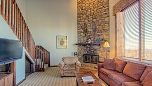 A living room with a stone fireplace, a television, a sofa, and a patterned armchair.