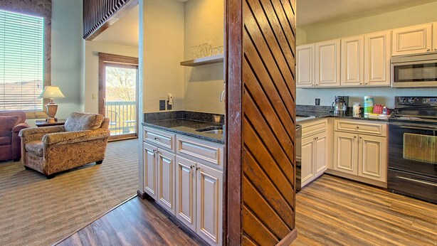 A spacious kitchen with white cabinets, a large island, and a wooden staircase.