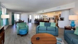Ein geräumiges Wohnzimmer mit einem blauen Sofa, einem grün gemusterten Sessel und einem Holztisch.
