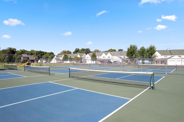 A tennis court with a net, surrounded by a fence, and residential buildings in the background. - Spacious Lodge w/ Sauna, Golf Views & Lake Access (Onamia)