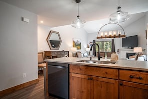 A kitchen with wooden cabinets, a dishwasher, a sink, pendant lights, and a large mirror.