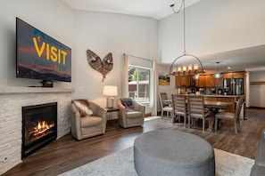 A living room with a fireplace, leather chairs, a dining area, and a kitchen.