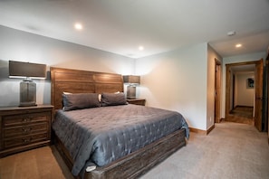 A bedroom with a large bed, wooden headboard, two bedside tables with lamps, and a carpeted floor.
