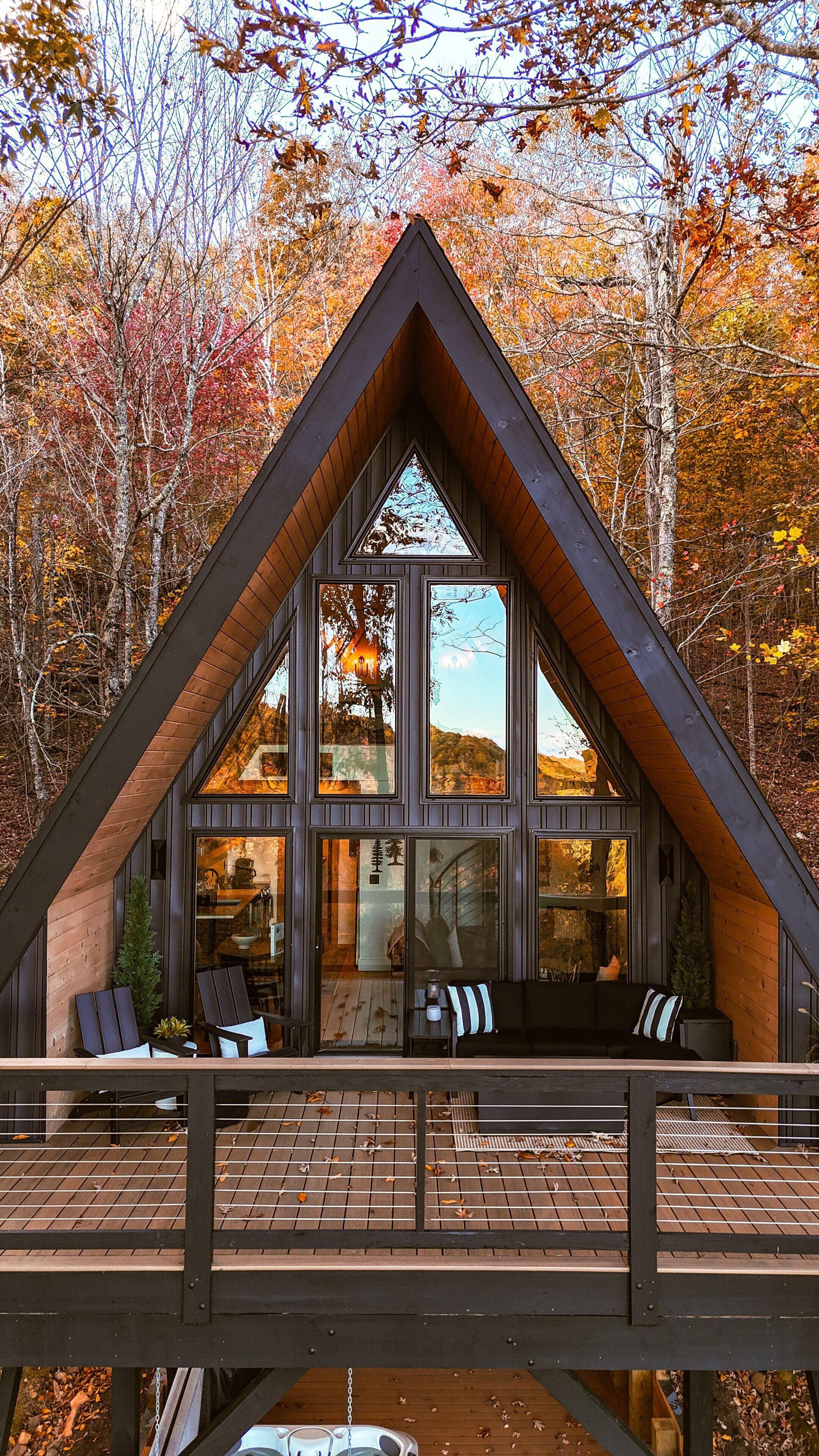 Una cabaña con techo triangular, ventanas amplias y una terraza con asientos.