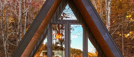 Una cabaña con techo triangular, ventanas amplias y una terraza con asientos.