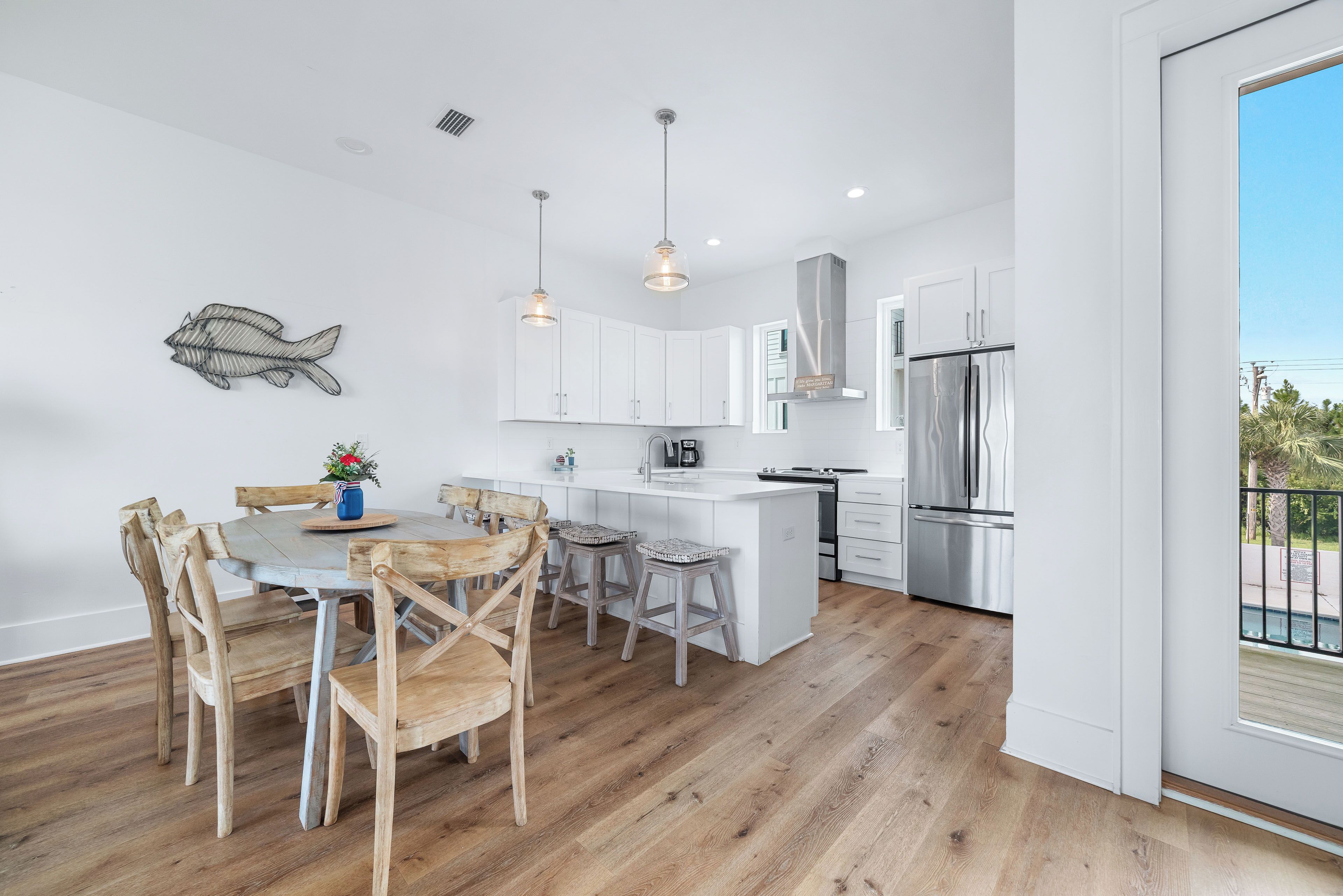A modern kitchen with white cabinetry, a stainless steel refrigerator, and a dining area with wooden chairs and a table.