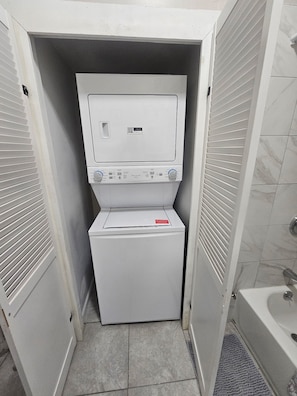 Uma lavanderia compacta com máquina de lavar e secar de abertura frontal, uma pequena janela e chão de azulejos.