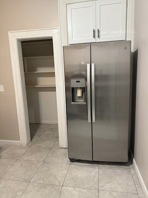 A stainless steel refrigerator with a water dispenser, located in a kitchen with a tiled floor and white cabinetry.