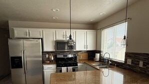 Una cocina moderna con armarios blancos, electrodomésticos de acero inoxidable, encimeras de granito e iluminación colgante.