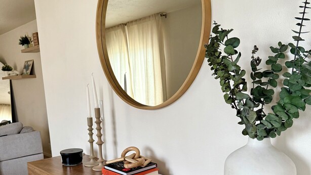 Una consola de madera con un espejo, libros, velas y una planta.