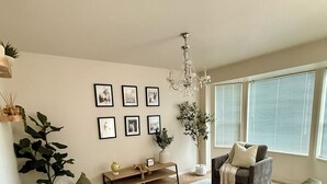 Una sala de estar con sofá, sillón y una mesa de centro. Se observan cuadros enmarcados en la pared y una araña.
