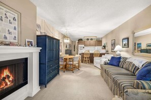 A living room with a fireplace, a dining area, and a kitchen in the background. - Sunny Delighthouse – Ocean View & Beach Access (Lincoln City)