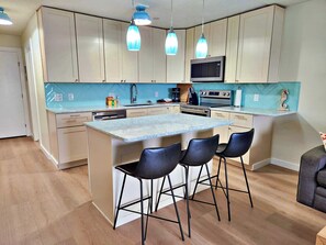 A modern kitchen with a central island, bar stools, and pendant lighting.