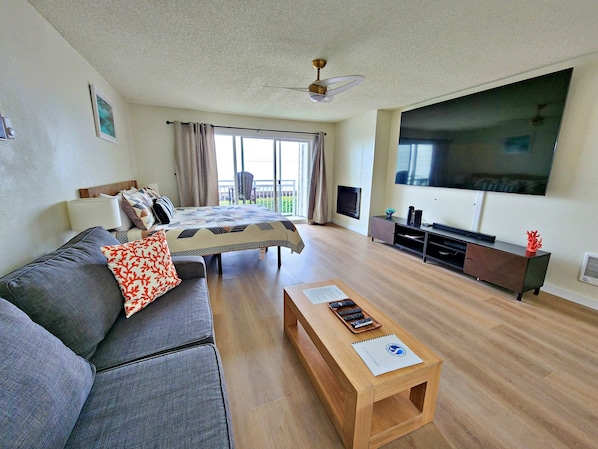 A modern living room with a sofa, a coffee table, a TV, and a balcony with curtains.