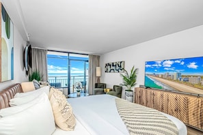 A hotel room with a large bed, a balcony with a view, a television, and artwork on the walls.