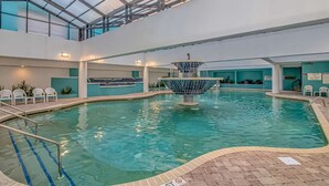 Piscina interna com uma fonte central, rodeada por áreas de estar e teto de vidro.