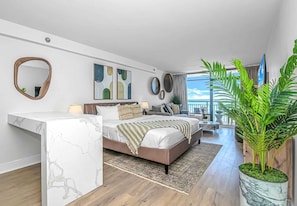 A modern bedroom with a marble vanity, a bed with multiple pillows, a sofa, and a large potted plant.