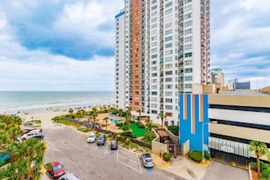 A high-rise hotel with a parking lot, a beach view, and a blue building adjacent to it.