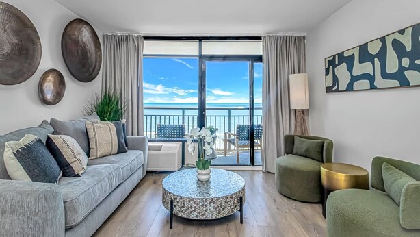 Uma sala de estar moderna com uma varanda, uma mesa de centro redonda e vista para o mar.