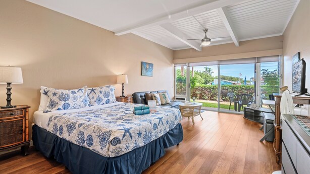 A spacious bedroom with a large bed, a desk, and a view of the outdoors. - KBS A106 - Updated Studio next to Beach (Kihei)