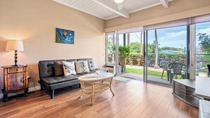 A spacious living room with a black sofa, a round wooden coffee table, and a wicker side table. - KBS A106 - Updated Studio next to Beach (Kihei)