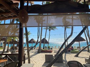 A beachside lounge with thatched umbrellas, lounge chairs, and a view of the ocean.