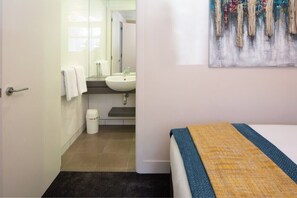 A bedroom with a bed, a bathroom visible through an open door, and a painting on the wall. - 2BR Lakefront Apt in Queenstown | Wi-Fi & Parking (Queenstown)