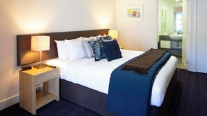 A hotel room with a bed, bedside tables, a lamp, a picture on the wall, and a bathroom visible through an open door. - 2BR Lakefront Apt in Queenstown | Wi-Fi & Parking (Queenstown)