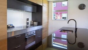 A modern kitchen with a stainless steel countertop, built-in oven, and a window with a view of a pink building. - 2BR Lakefront Apt in Queenstown | Wi-Fi & Parking (Queenstown)