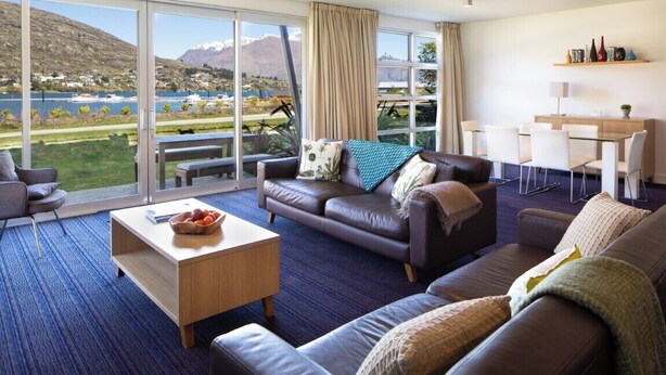 A modern living room with a large sliding glass door leading to a scenic view of mountains and a lake. - 2BR Lakefront Apt in Queenstown | Wi-Fi & Parking (Queenstown)