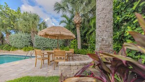 Eine Terrasse im Freien mit Pool, Holzmöbeln und einem Reetdachschirm.