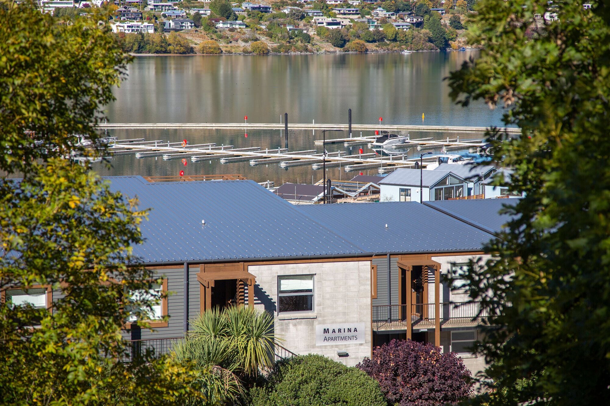 A marina with docked boats, a building labeled 'MARINA APARTMENTS' with a view of the water, and surrounding greenery.