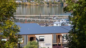 Een jachthaven met liggende boten, een gebouw met de tekst 'MARINA APARTMENTS' en uitzicht op het water, omgeven door groen.