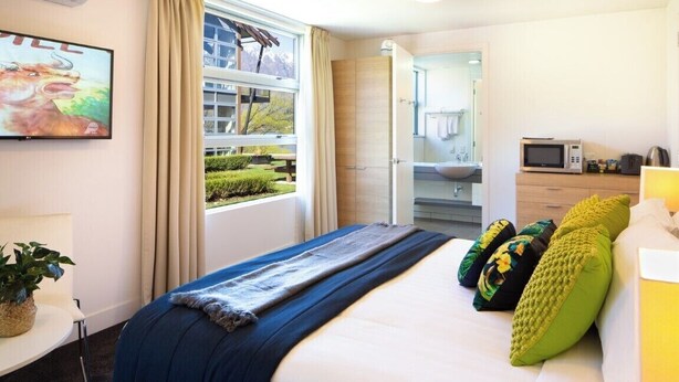 Een hotelkamer met een bed, een televisie, een raam met gordijnen, een badkamer en een kitchenette.