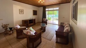 A spacious living room with a wooden ceiling, a large window with a view of greenery, a television, and a seating area with a sofa and chairs. - Peaceful house by the sea (Îles Sous-le-Vent)