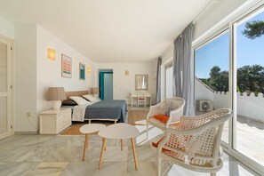 Une chambre bien éclairée, avec un lit, des tables de chevet, un bureau et une chaise. Une grande fenêtre, ornée de rideaux, laisse entrer la lumière, et la pièce présente un design moderne.