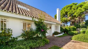 A white building with a tiled roof, a brick pathway, and lush greenery.