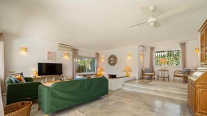 A spacious living area with a flat-screen TV, green sofa, and a ceiling fan.