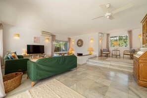 A spacious living area with a flat-screen TV, green sofa, and a ceiling fan.