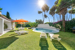 A backyard with a swimming pool, sun loungers, and a red umbrella.