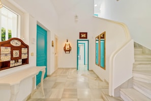 A hallway with a staircase, a wooden cabinet with drawers, a door with a light switch, and a wall-mounted light fixture.