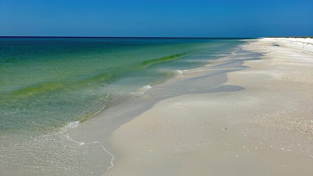 A beach with clear turquoise water and a wide sandy shore under a bright blue sky.