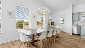 A modern kitchen with a dining area, featuring a large wooden table, white chairs, and a chandelier.